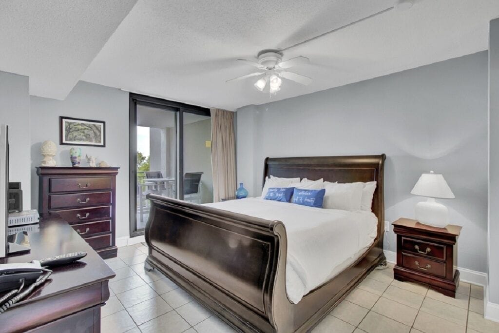 A bedroom with a large bed, a desk, a dresser, a nightstand, and a ceiling fan.