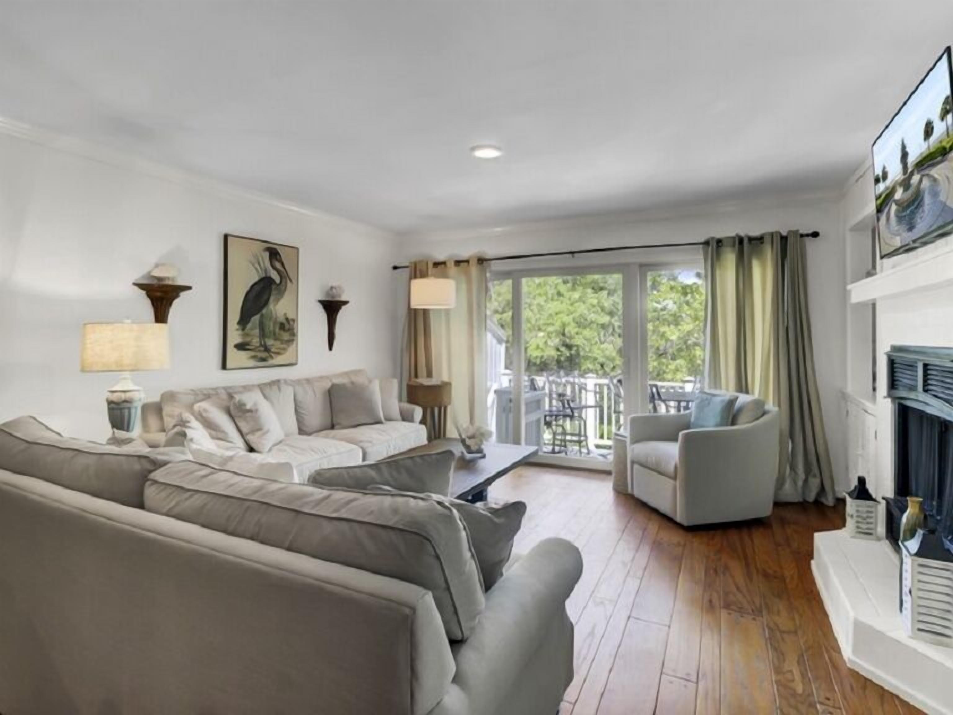 A living room with a sofa, a chair, a table, and a balcony with curtains.