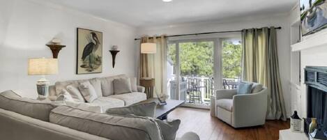 A living room with a sofa, a chair, a table, and a balcony with curtains.