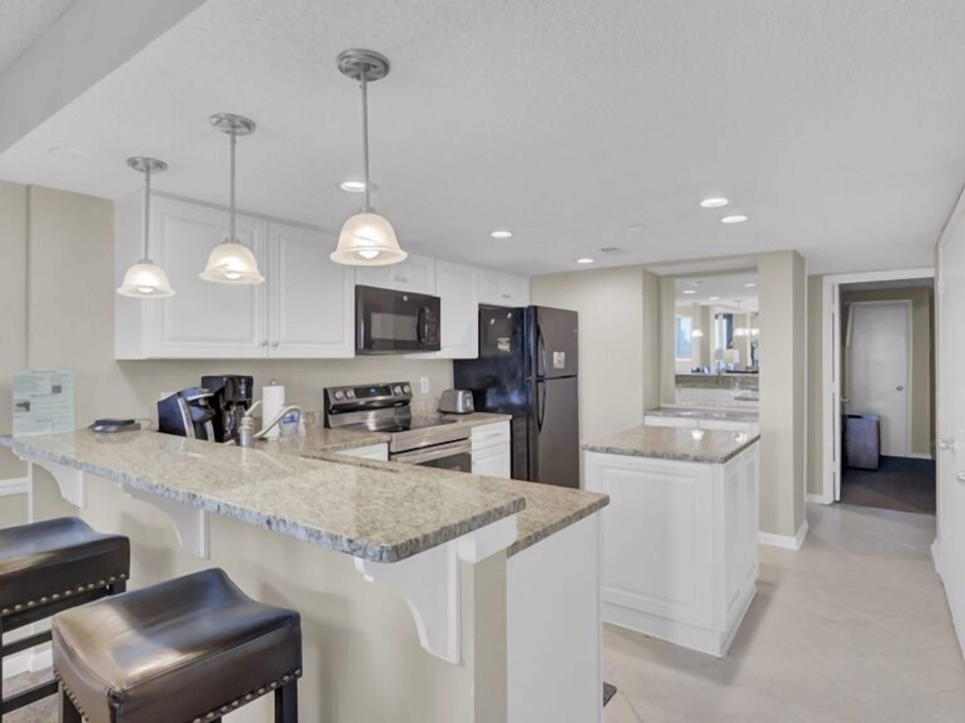 A modern kitchen with granite countertops, stainless steel appliances, and pendant lighting.