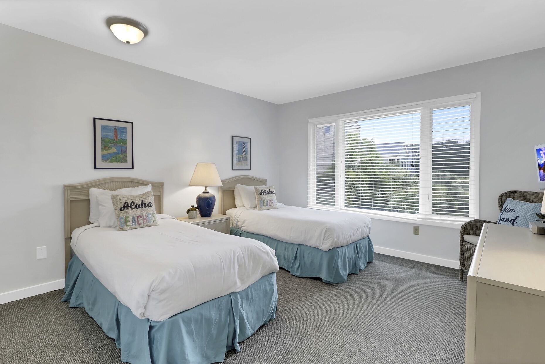 A bedroom with two beds, a desk, a lamp, and a window with blinds.