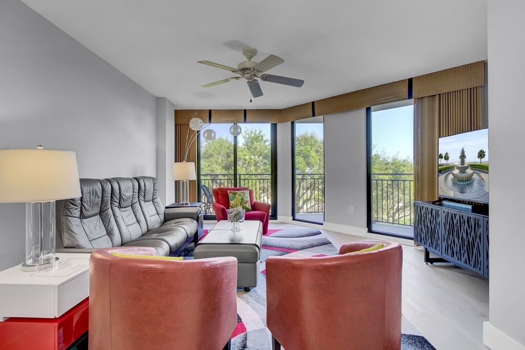 A modern living room with a sofa, armchairs, a TV, and a balcony with a view.