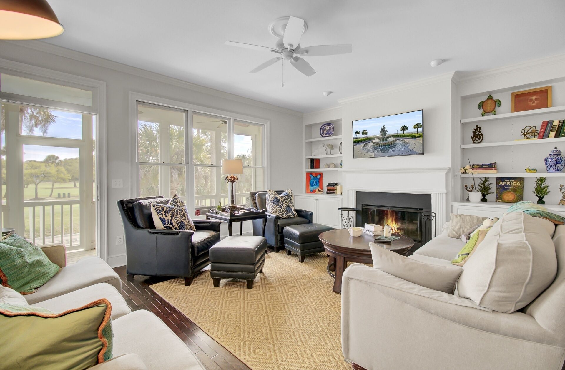 A spacious living room with a fireplace, large windows, and a ceiling fan.