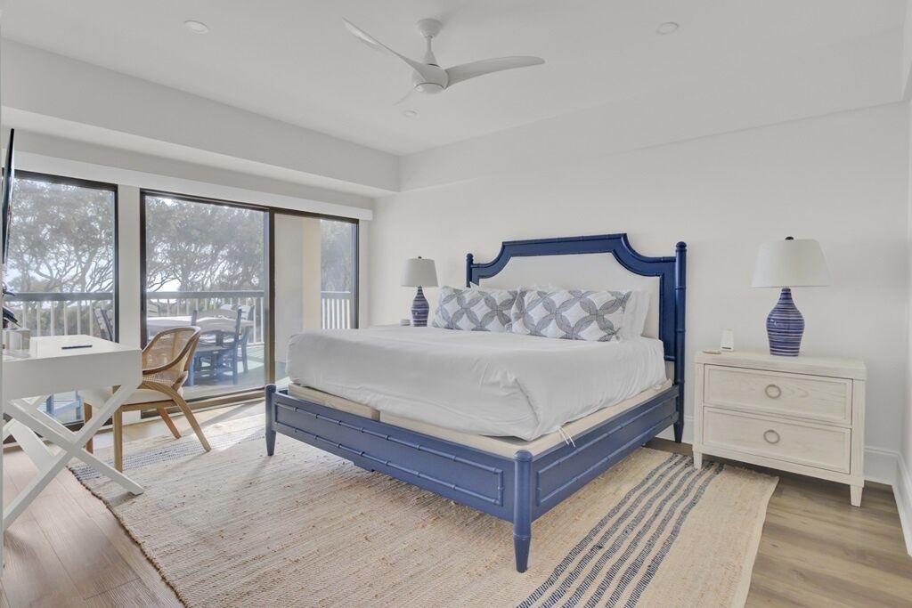 A bedroom with a bed, a desk, a chair, a nightstand, and a ceiling fan.