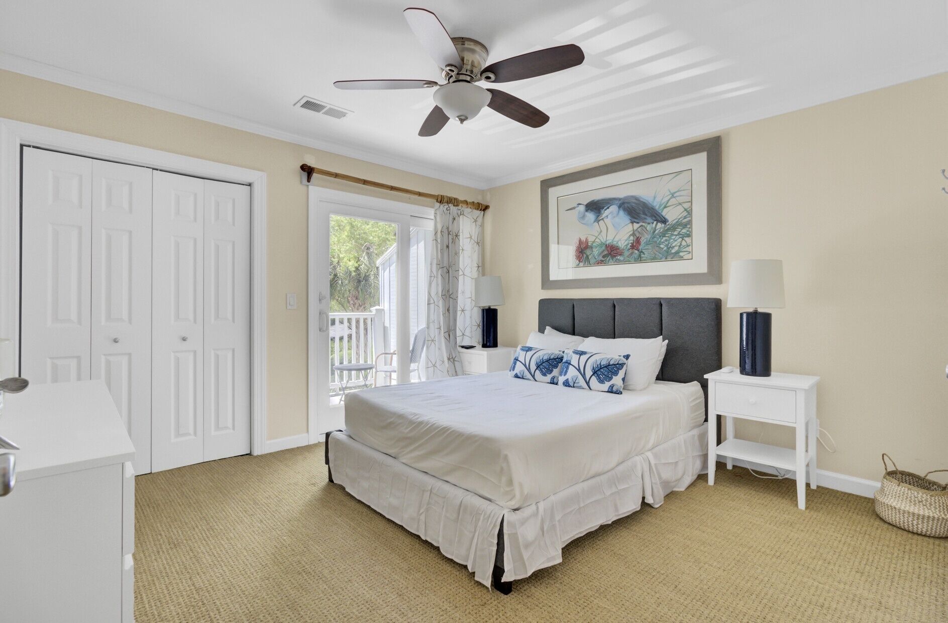 A bedroom with a bed, a ceiling fan, a nightstand, a lamp, a framed picture, and a door.