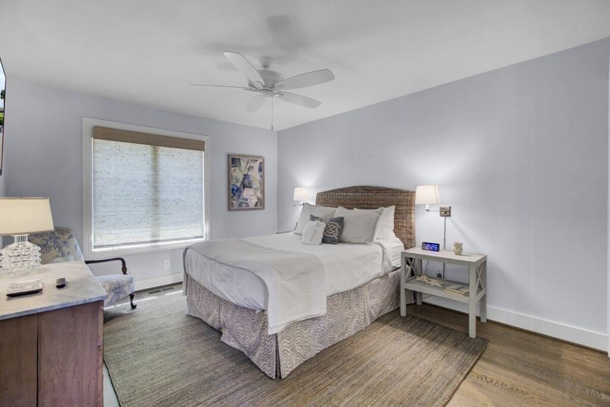 Un dormitorio con cama, mesitas de noche, escritorio, silla, ventana y ventilador de techo.