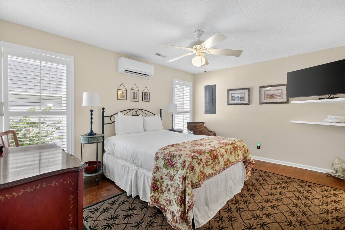 A bedroom with a bed, a ceiling fan, a TV, and framed pictures on the wall.