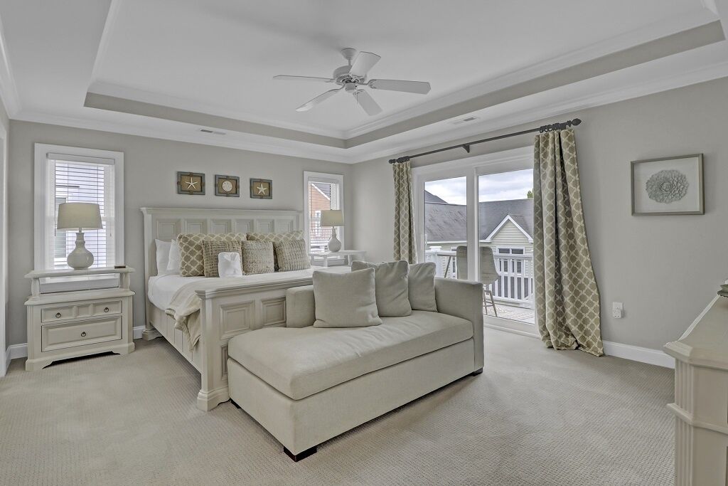 A bedroom with a bed, a white sofa, a nightstand, a ceiling fan, and a window with curtains.