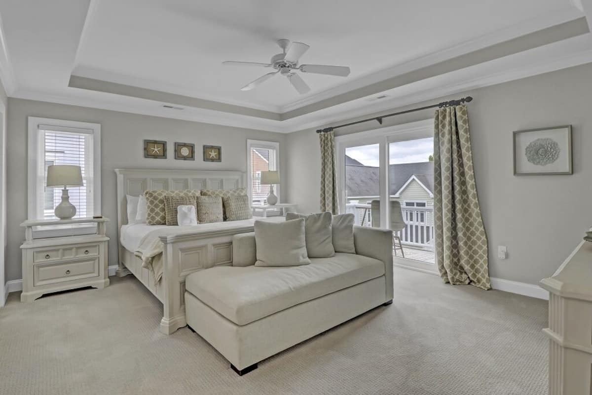 A bedroom with a bed, a white sofa, a nightstand, a ceiling fan, and a window with curtains.