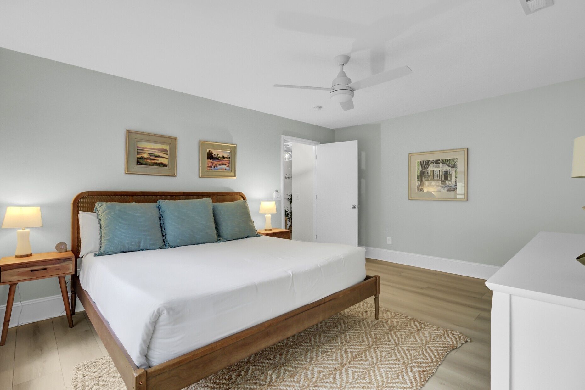A bedroom with a bed, bedside lamps, a ceiling fan, and framed pictures on the walls.