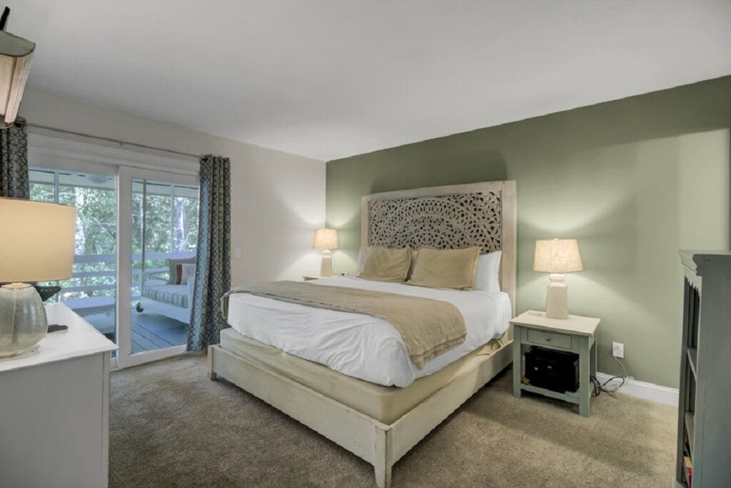 A bedroom with a bed, bedside tables, a lamp, and a view of the outdoors.