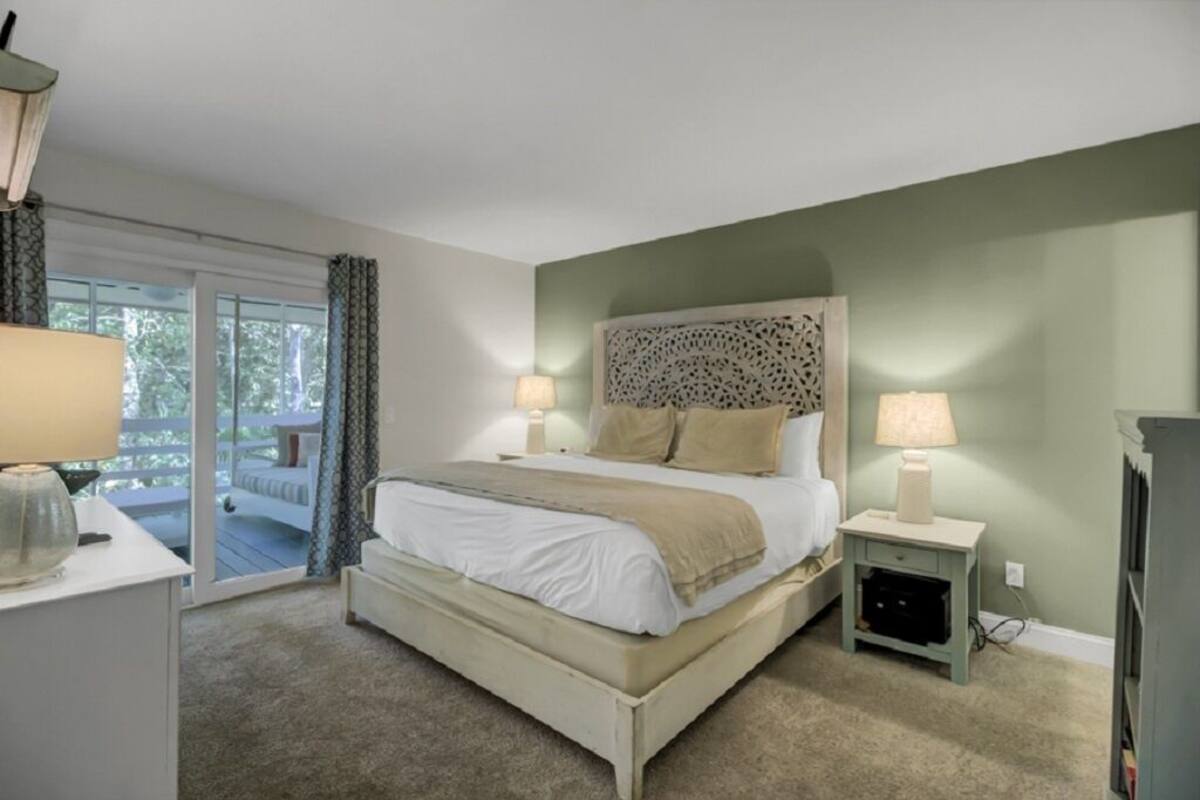 A bedroom with a bed, bedside tables, a lamp, and a view of the outdoors.