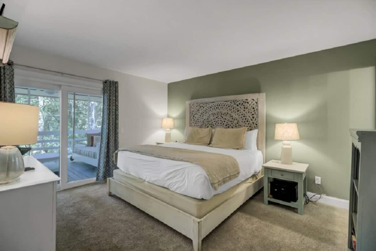 A bedroom with a bed, bedside tables, a lamp, and a view of the outdoors.