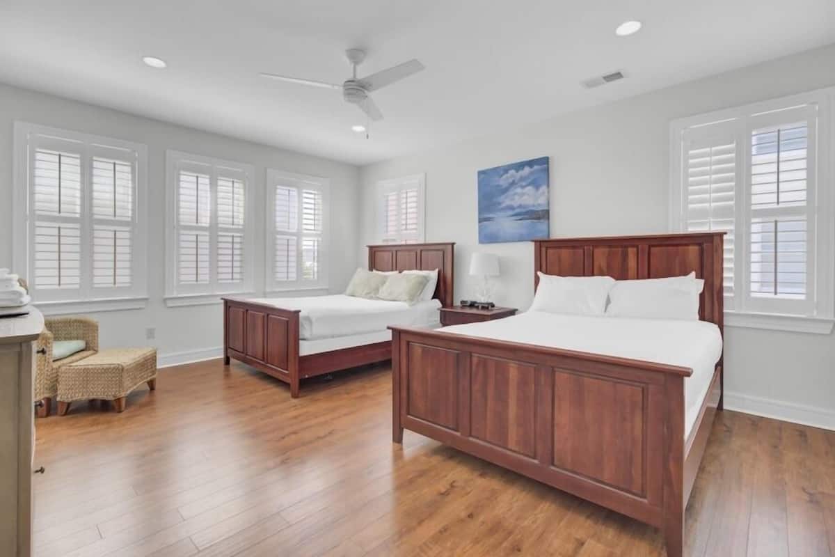A bedroom with two wooden beds, a ceiling fan, and a large window with shutters.