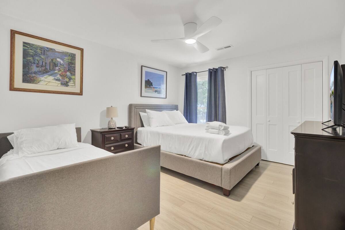 A hotel room with two beds, a nightstand, a ceiling fan, and a television.