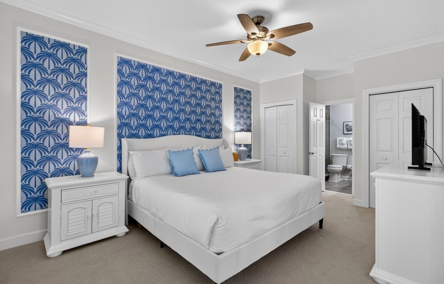 A bedroom with a bed, nightstands, a ceiling fan, and a bathroom visible through an open door.