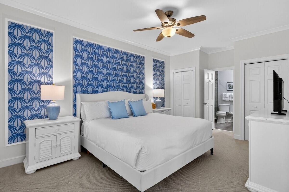 A bedroom with a bed, nightstands, a ceiling fan, and a bathroom visible through an open door.