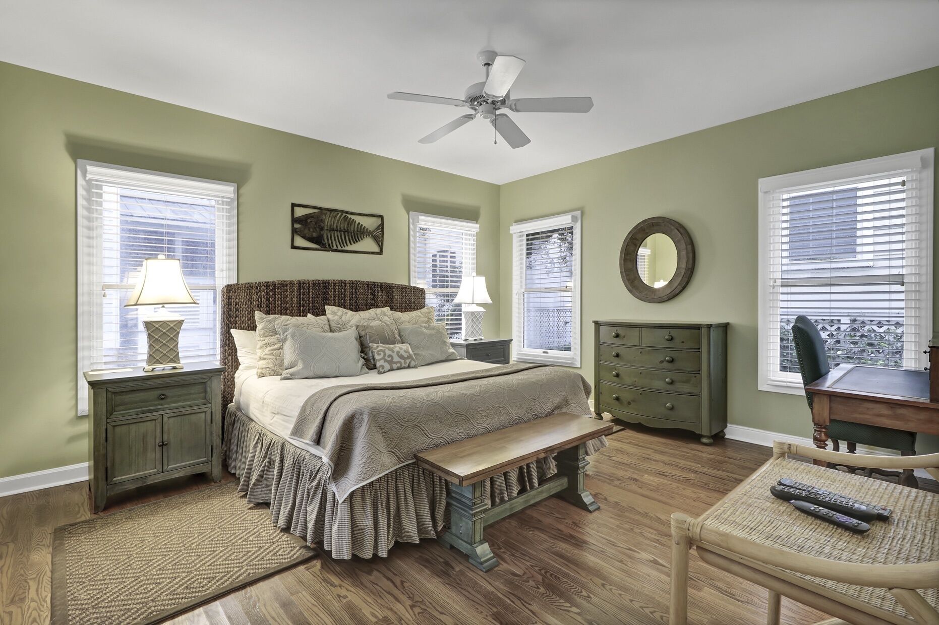 A bedroom with a bed, nightstands, a dresser, a chair, a desk, a ceiling fan, and windows with blinds.
