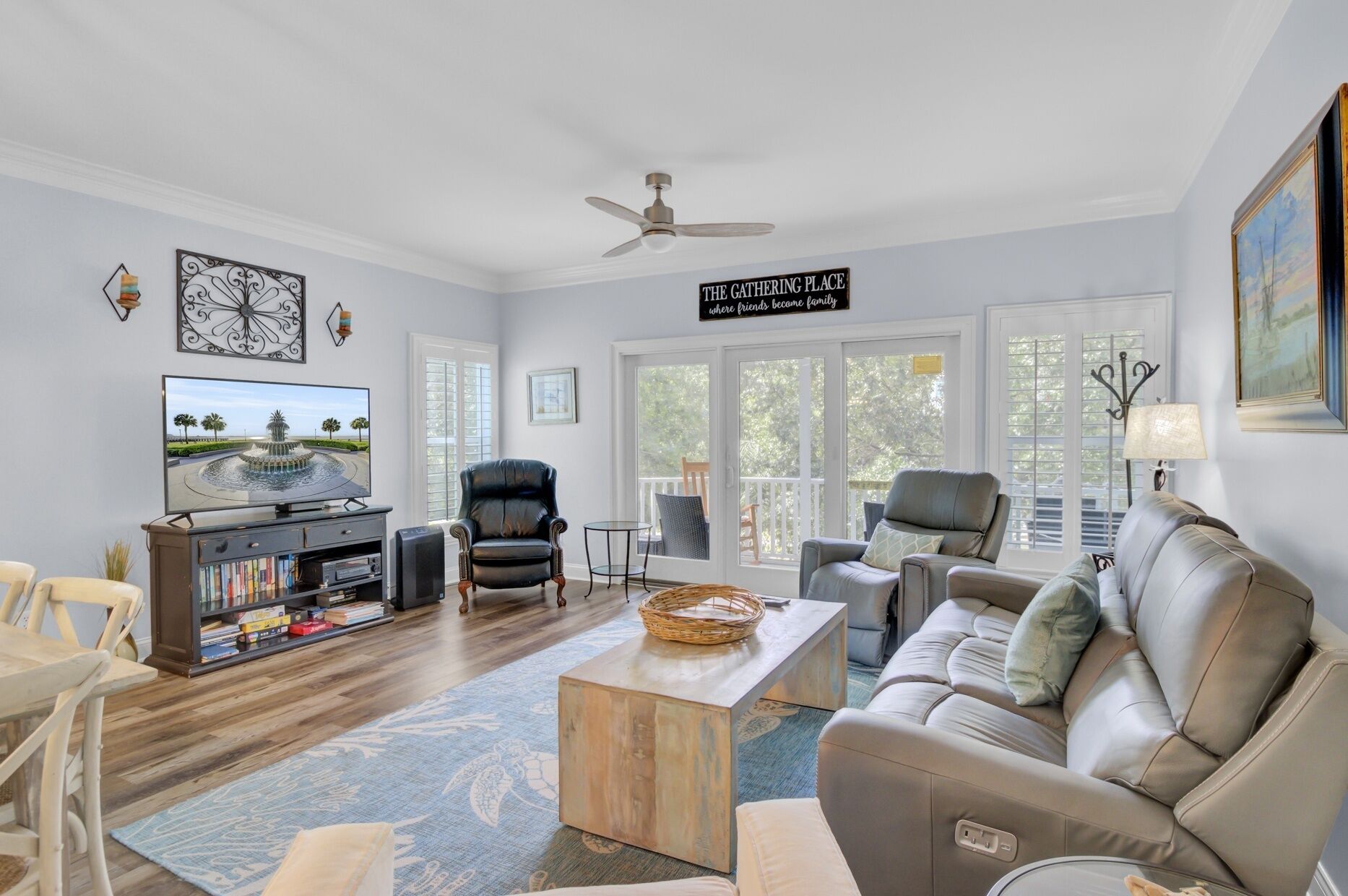 A living room with a TV, leather chairs, a coffee table, and a sign that reads 'The Gathering Place where friends become family.'
