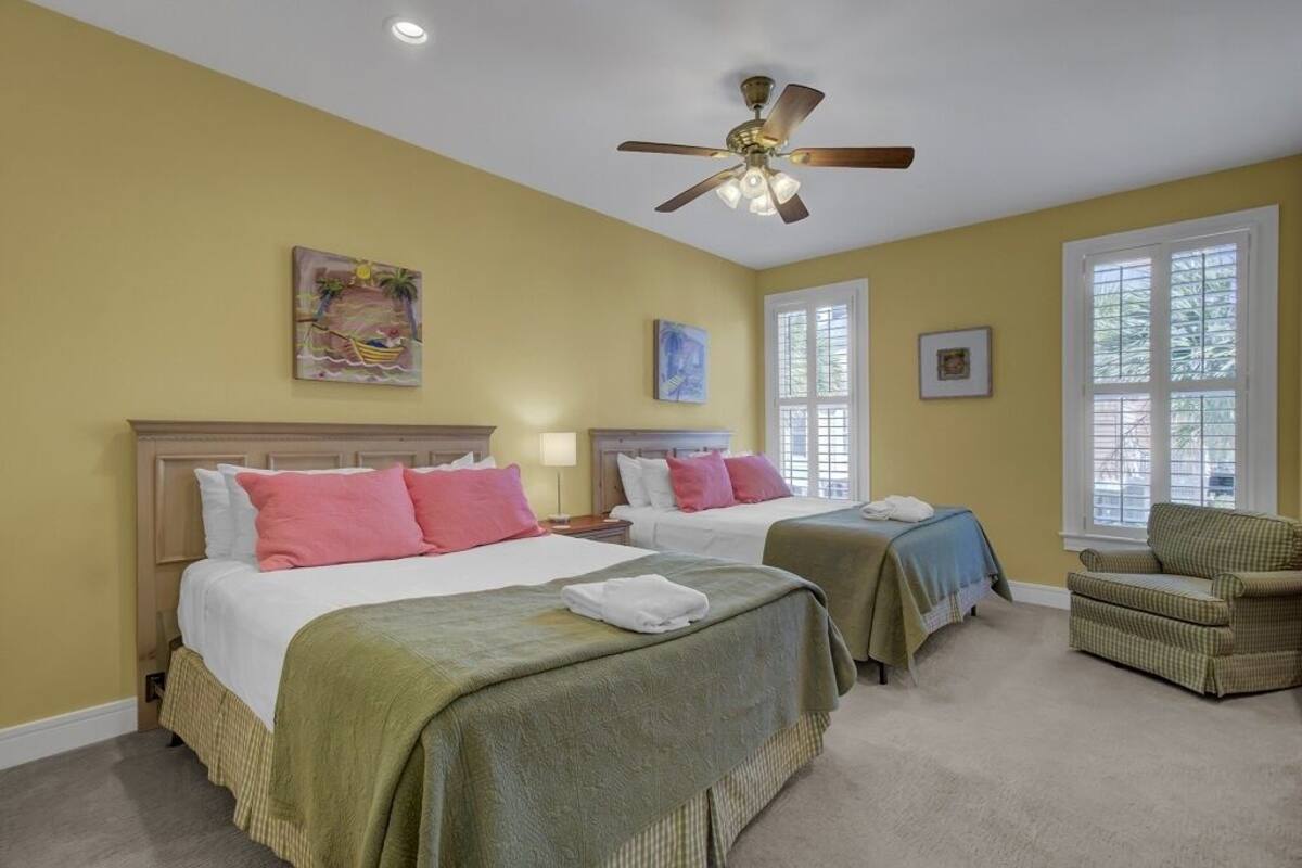 A hotel room with two beds, a ceiling fan, and large windows.