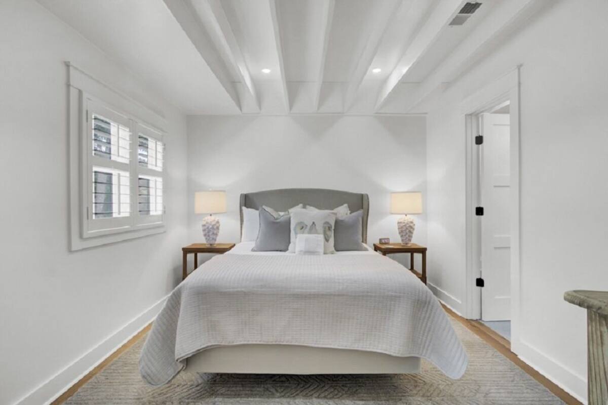A bedroom with a large bed, two bedside tables with lamps, a window, and a door.
