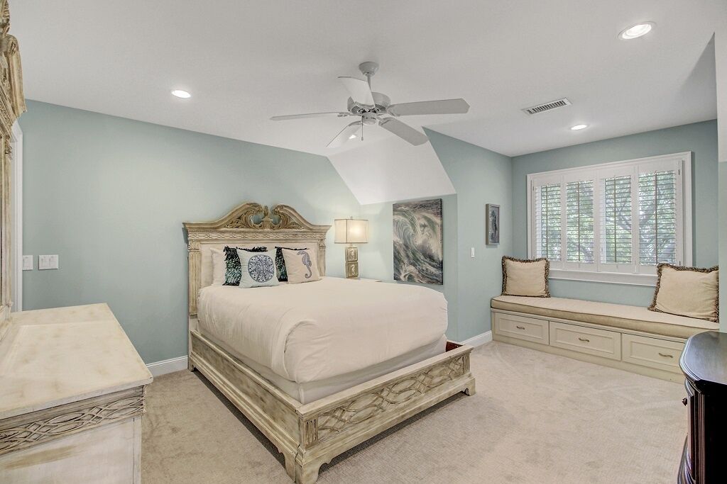 A bedroom with a bed, a ceiling fan, a window with blinds, and a built-in bench with storage drawers.