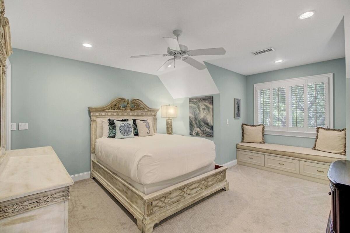 A bedroom with a bed, a ceiling fan, a window with blinds, a dresser, and a nightstand.