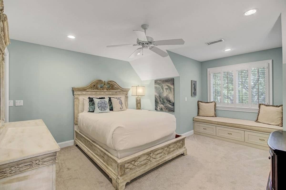 A bedroom with a bed, a ceiling fan, a window with blinds, and a built-in bench with storage drawers.