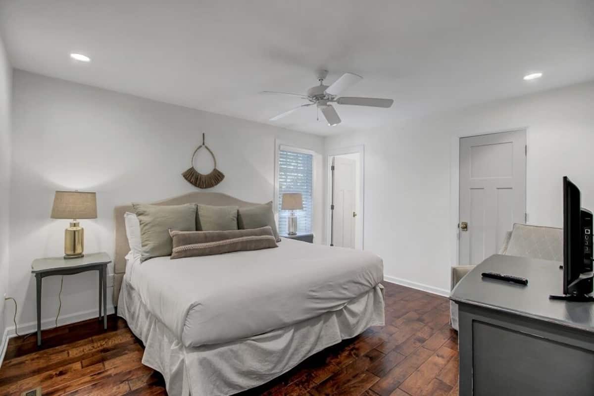 A bedroom with a bed, a desk, a ceiling fan, and a window with blinds.