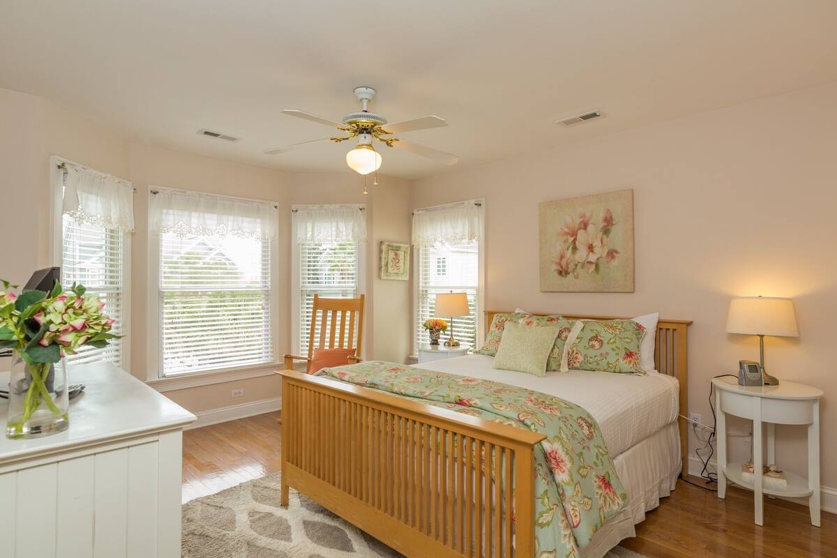 A bedroom with a wooden bed, a ceiling fan, a bedside table, a nightstand, and a window with blinds.