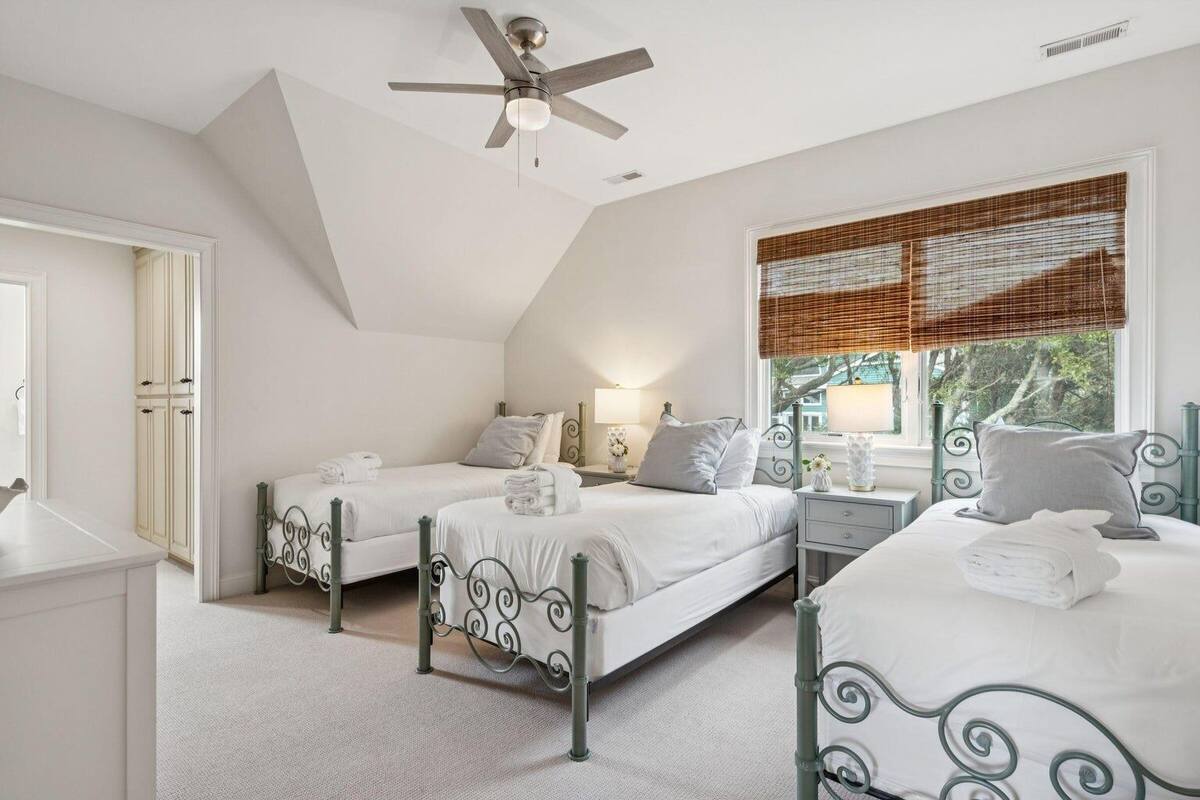 A bedroom with two beds, a ceiling fan, a window with blinds, and a nightstand with a lamp.