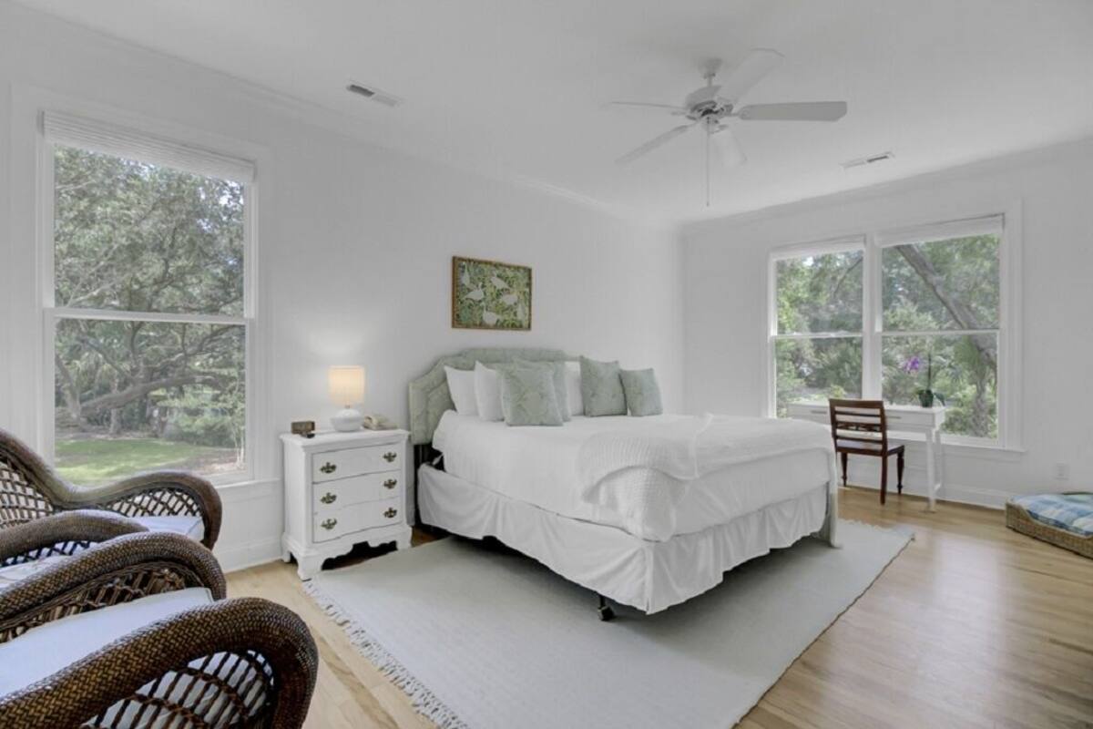 A bedroom with a bed, nightstands, a chair, and large windows.