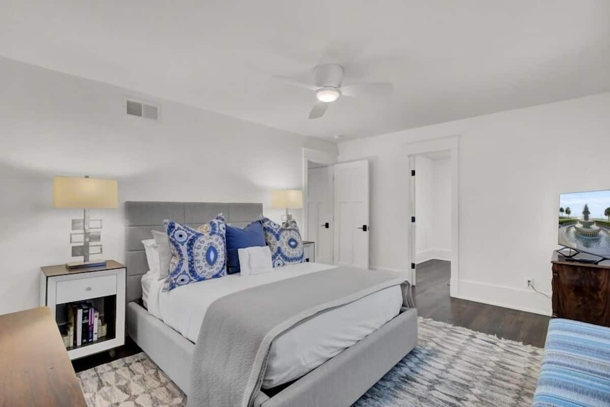 A bedroom with a bed, nightstands, a ceiling fan, a bookshelf, and a view of a fountain.