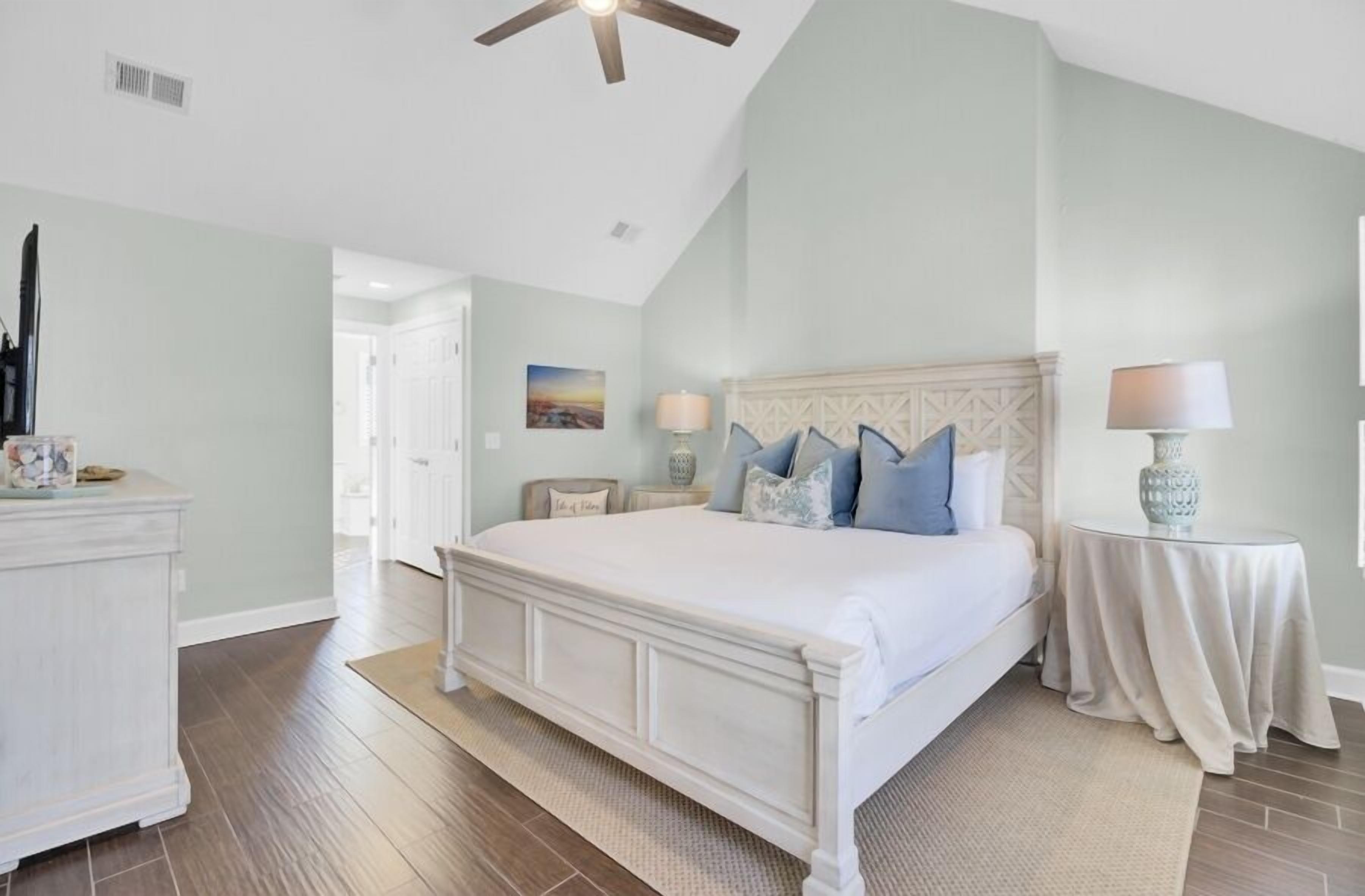 A bedroom with a large bed, a ceiling fan, a nightstand, and a lamp.