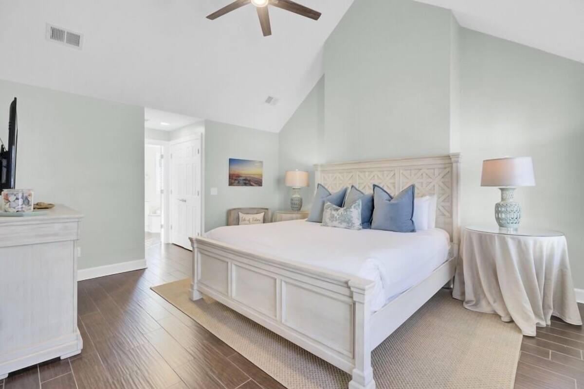 A bedroom with a large bed, a ceiling fan, a nightstand, and a lamp.