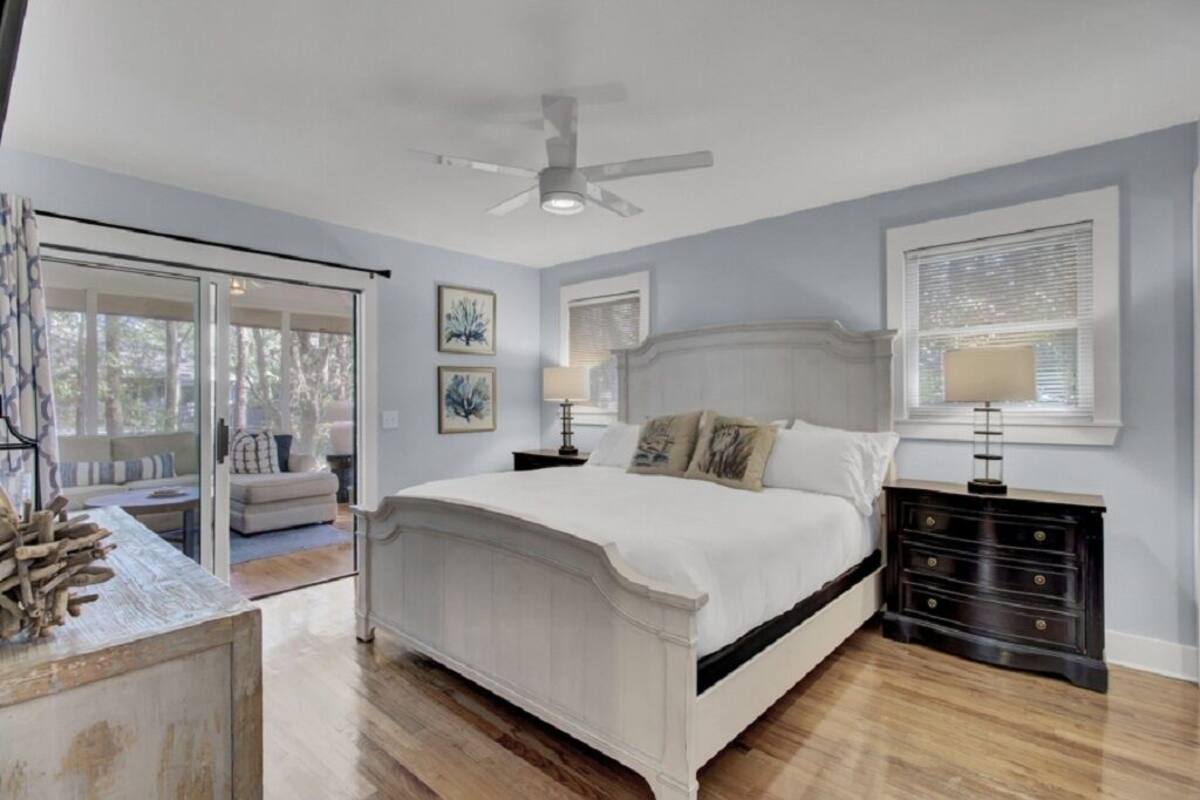 A bedroom with a bed, a nightstand, a ceiling fan, and a window with blinds.