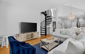 A modern living room with a flat-screen TV, a blue sofa, a white sofa, a wooden coffee table, and a staircase leading to an upper level. - Wild Dunes Vaction Homes 3&4 Bedrooms (Isle of Palms)