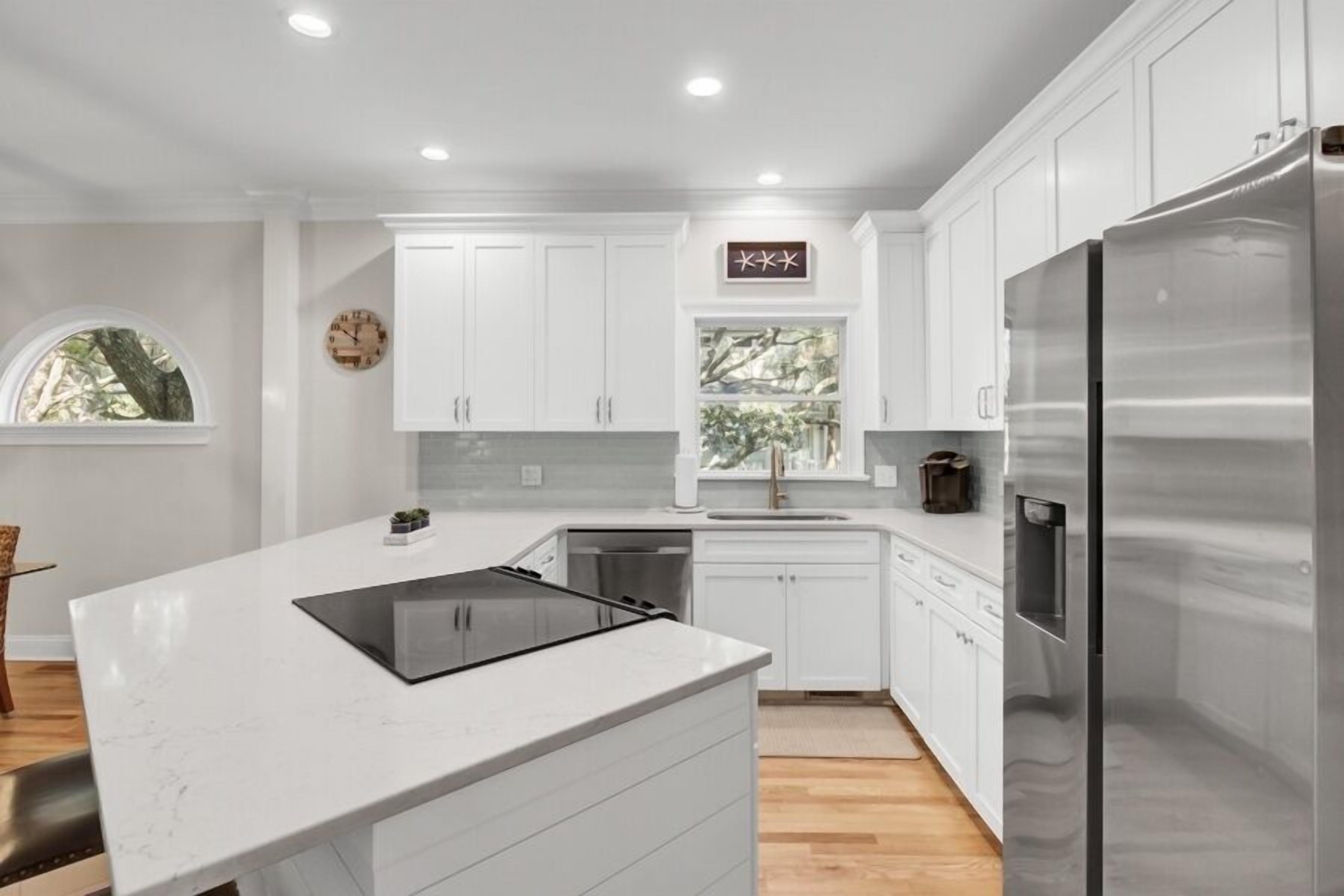 A modern kitchen with white cabinetry, a stainless steel refrigerator, and a window with a view of trees.
