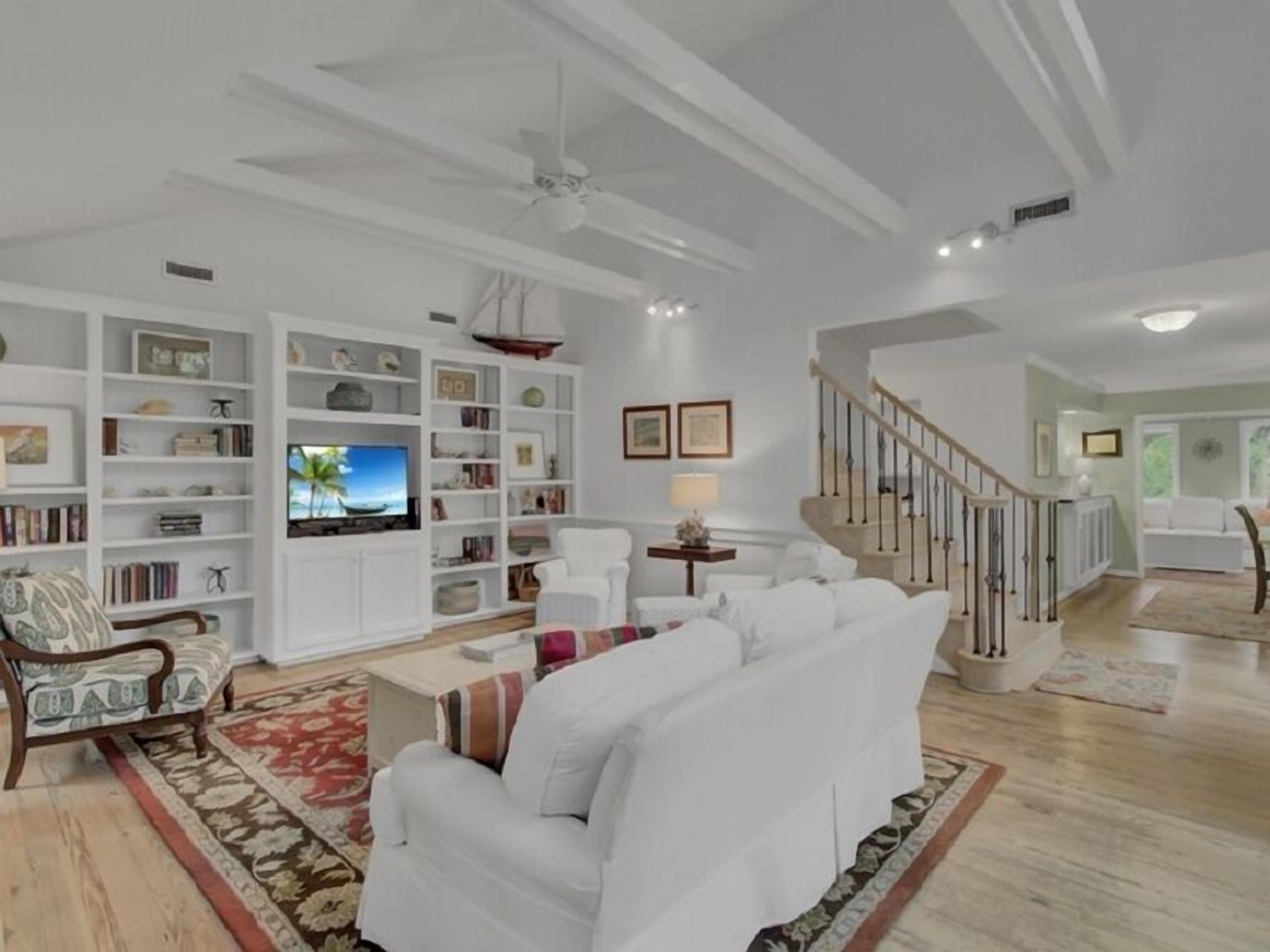 A spacious living room with a large white sofa, a television, and a bookshelf.