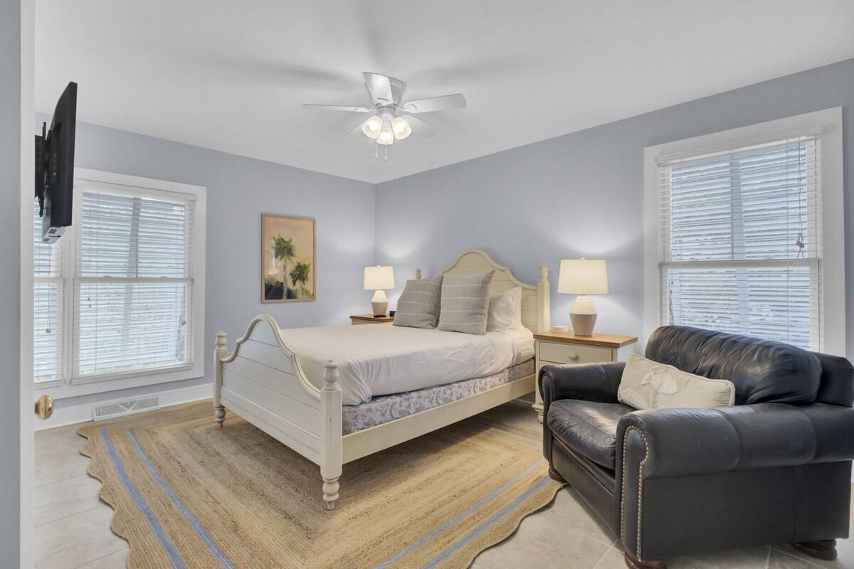 A bedroom with a bed, two bedside tables with lamps, a ceiling fan, and a black leather chair.