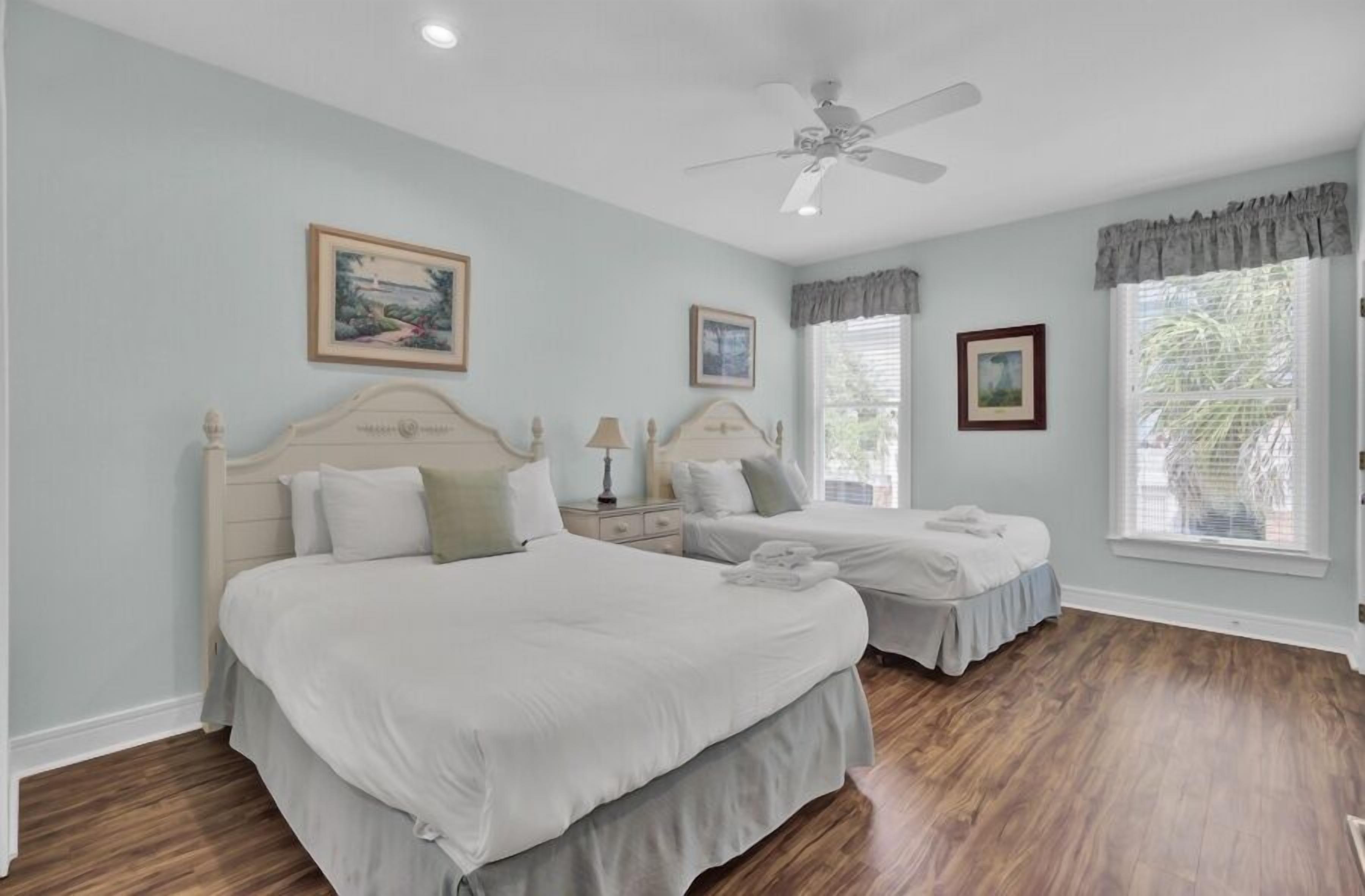 A bedroom with two beds, a ceiling fan, and framed artwork on the walls.
