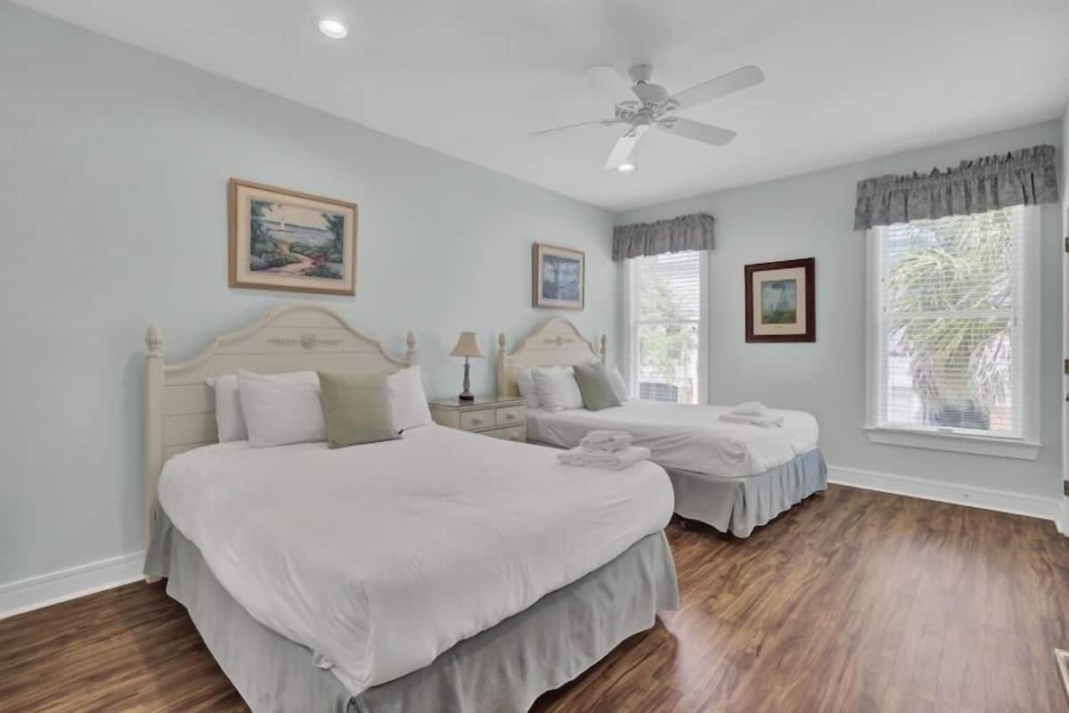 A bedroom with two beds, a ceiling fan, and framed artwork on the walls.