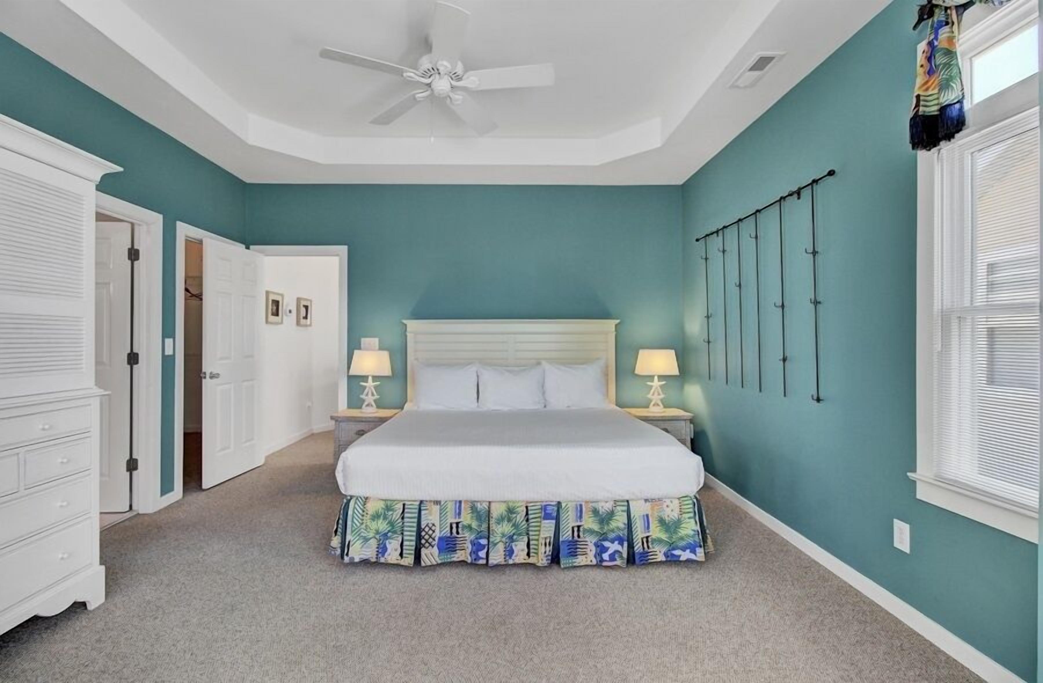 A bedroom with a bed, white nightstands, a ceiling fan, and a teal wall.