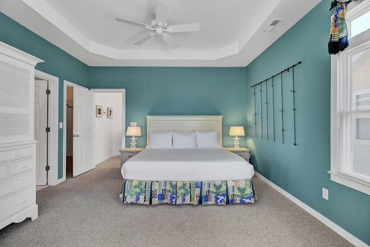 A bedroom with a bed, two bedside tables with lamps, a ceiling fan, and a window with blinds.
