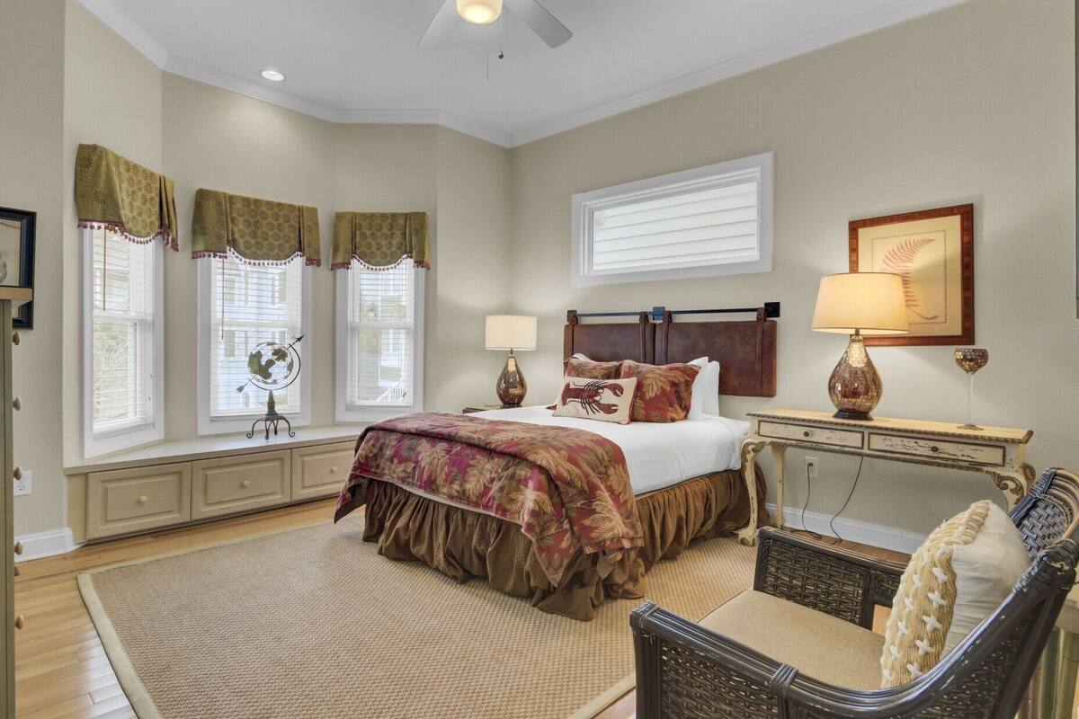 A bedroom with a bed, bedside lamps, a chair, a desk, and a window with curtains.