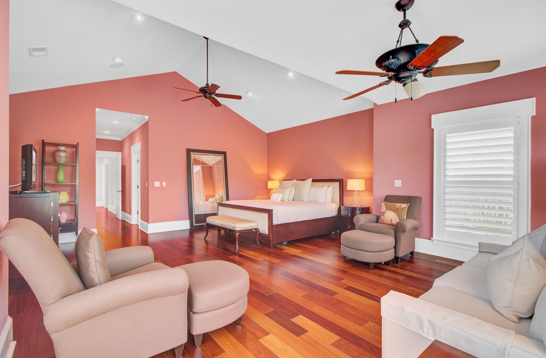 A spacious hotel room with a large bed, two ceiling fans, a sitting area with chairs, and a wooden floor.