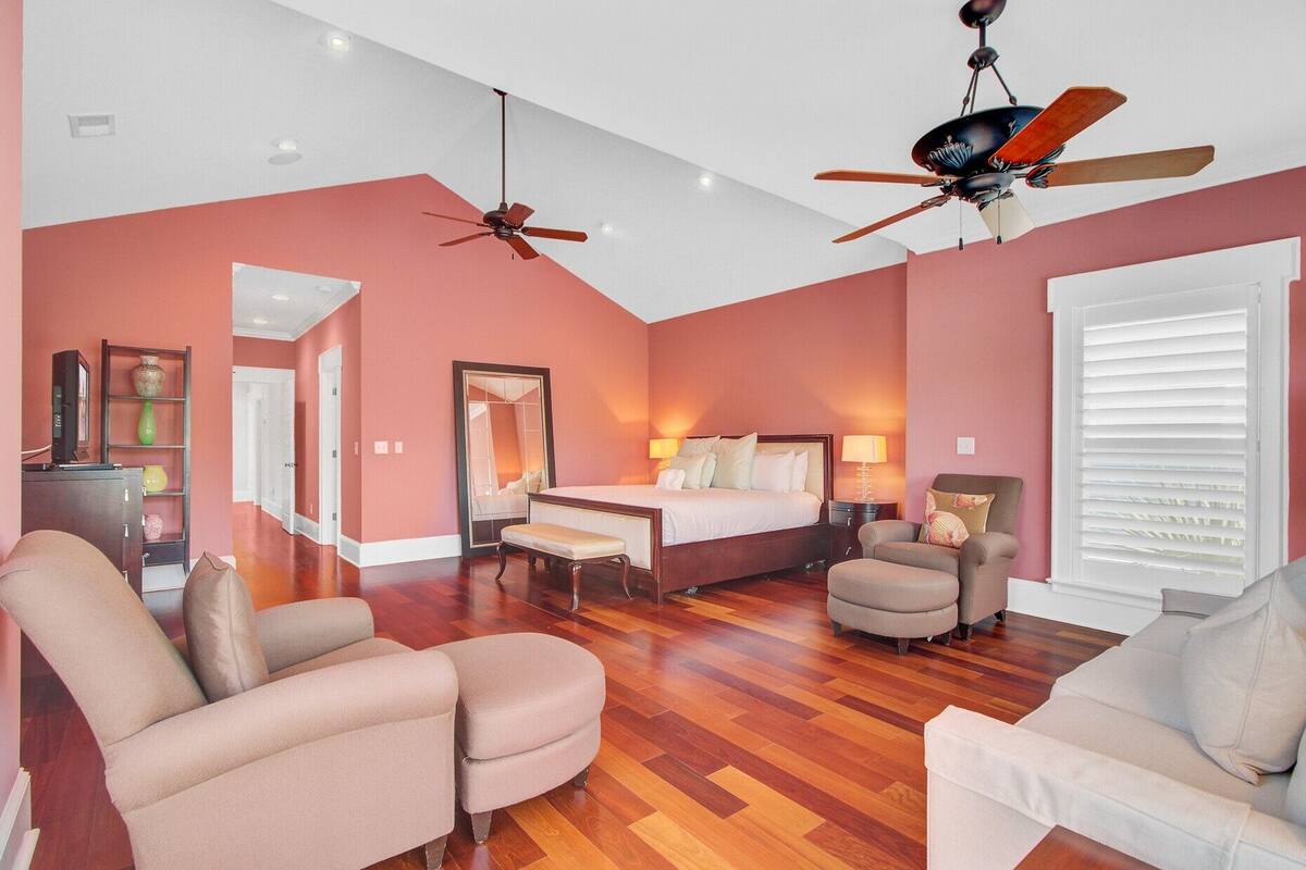 A hotel room with a bed, two chairs, a desk, a mirror, and two ceiling fans.