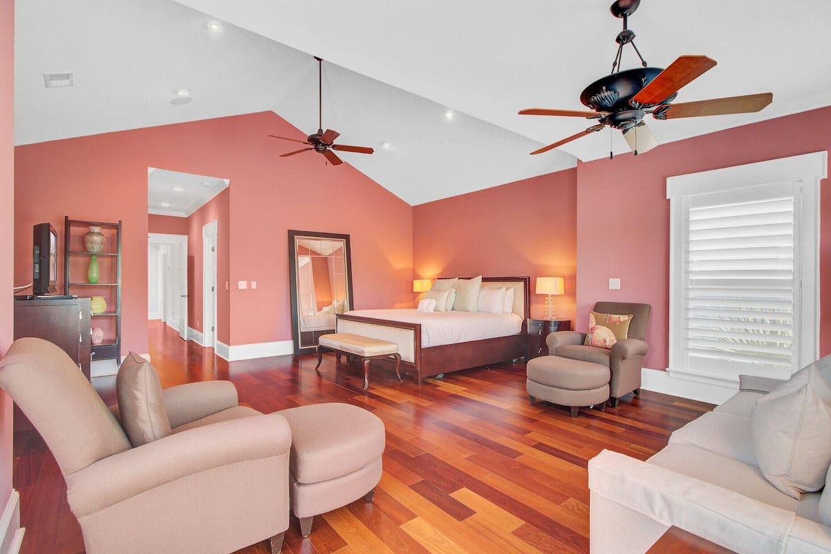 A spacious hotel room with a large bed, two ceiling fans, a sitting area with chairs, and a wooden floor.