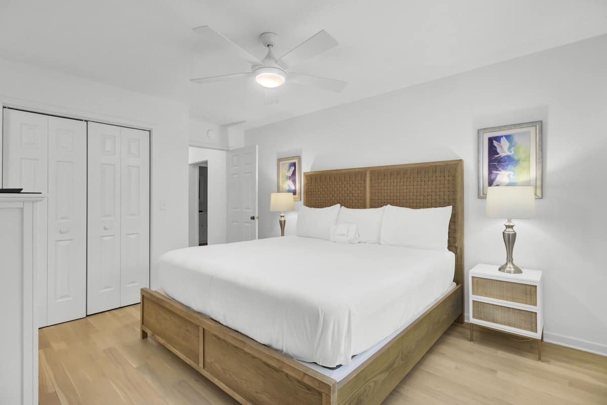 A bedroom with a bed, a ceiling fan, a nightstand, a lamp, and a door.