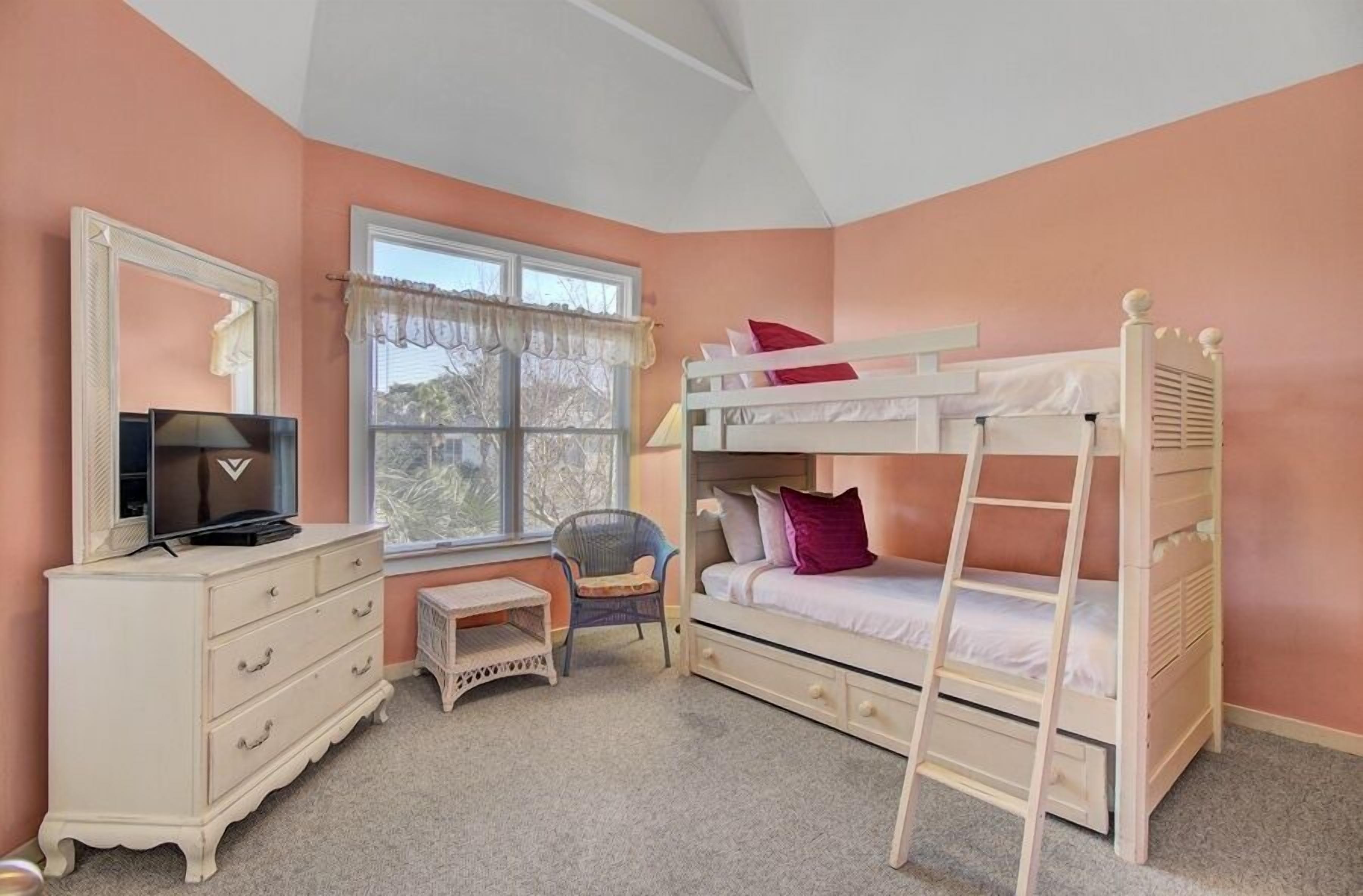 A bedroom with a bunk bed, a dresser, a chair, a small table, and a window with curtains.